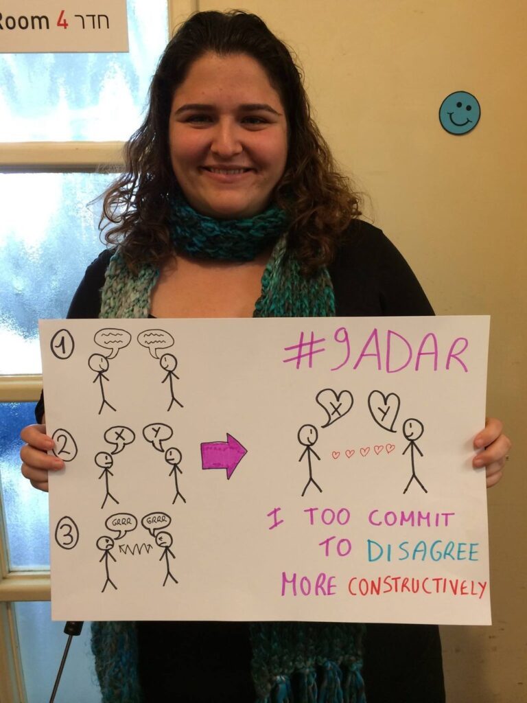 Woman holding a #9Adar sign about constructive disagreement