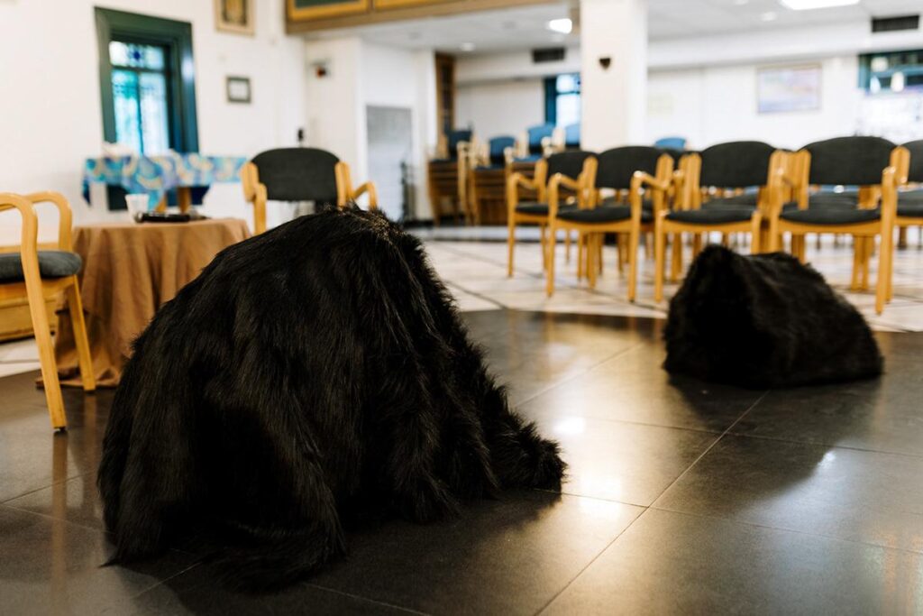 Dark draped sculptures on the floor of a hall with chairs