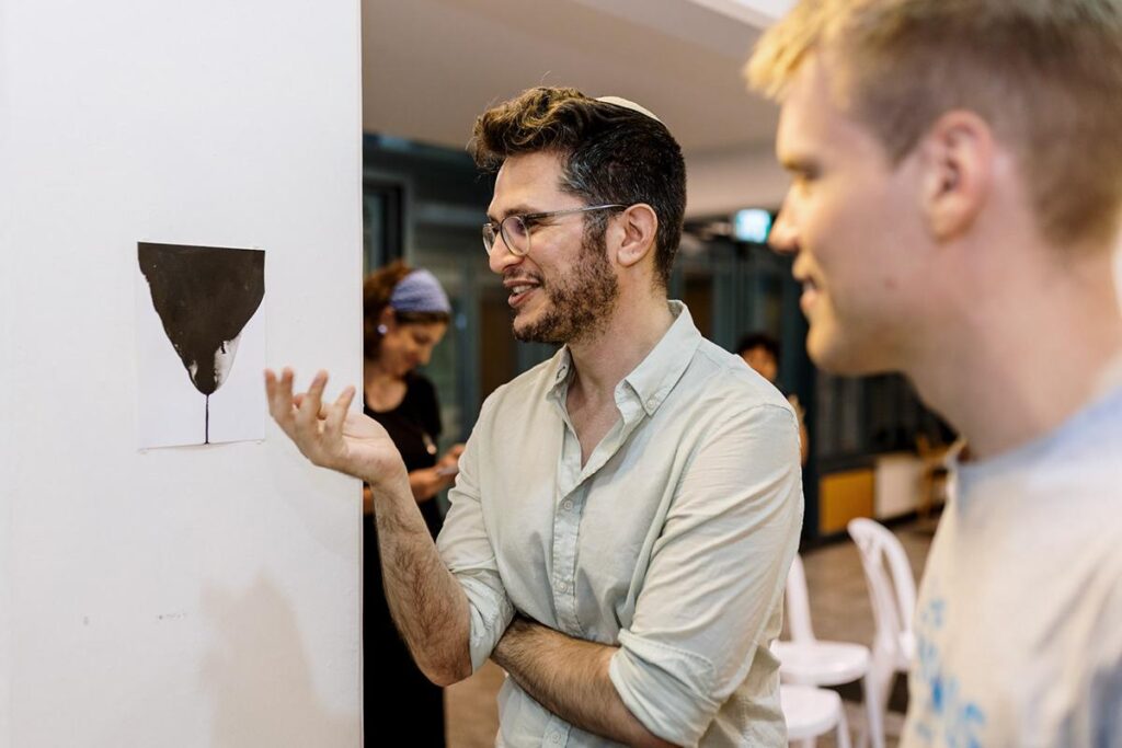 Two young men talking beside a wall-mounted artwork