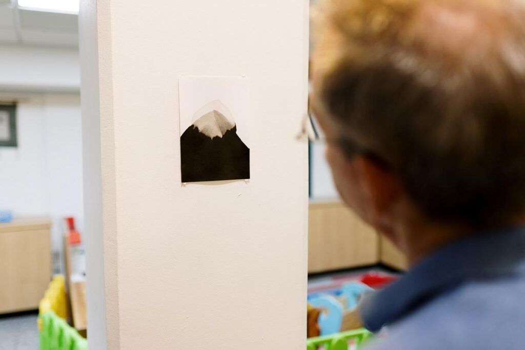 Man looking at a small dark object mounted on a white wall in a gallery